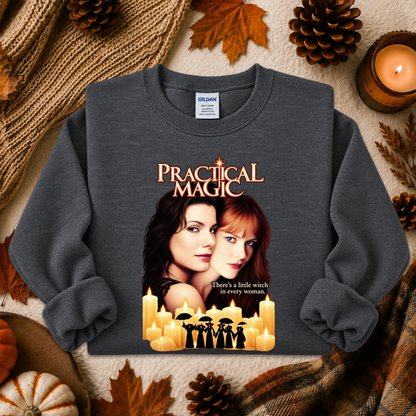 A dark gray crewneck sweatshirt featuring a 'Practical Magic' movie graphic, styled in a cozy autumn flat-lay with pinecones, leaves, a candle, and a knitted blanket.
