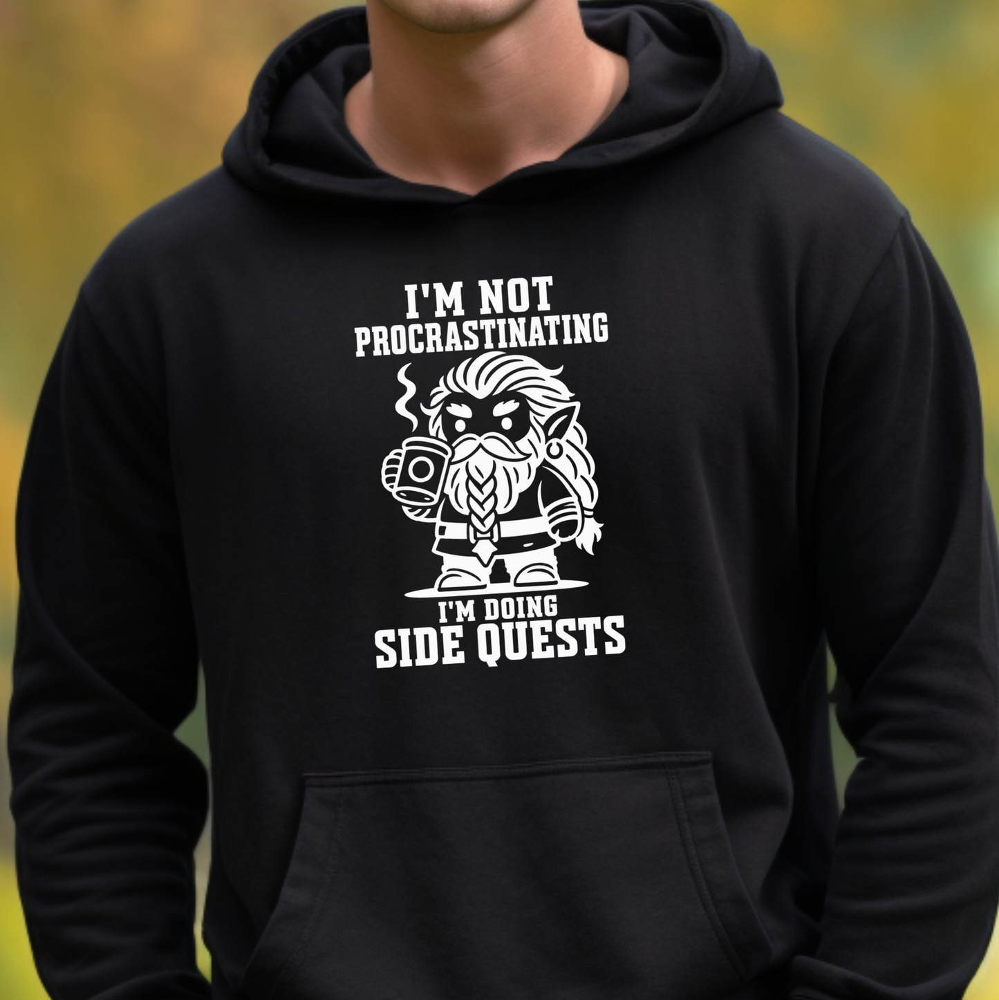 A person wearing a black pullover hoodie with a white graphic print that reads 'I'M NOT PROCRASTINATING I'M DOING SIDE QUESTS' around an illustrated bearded character, shown against a blurred outdoor background.