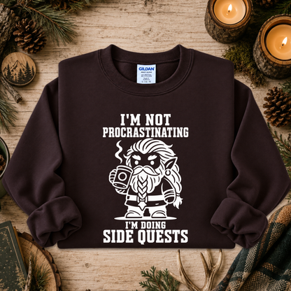 A dark brown crewneck sweatshirt with a white graphic of a Viking holding a mug and the text 'I'M NOT PROCASTINATING I'M DOING SIDE QUESTS', displayed on a rustic wooden background with pine needles, pinecones, and lit candles.