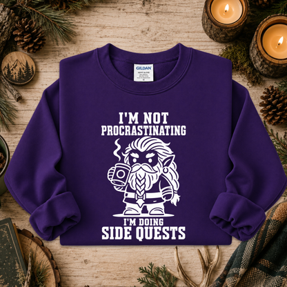 A purple crewneck sweatshirt with a white graphic and text reading 'I'M NOT PROCRASTINATING I'M DOING SIDE QUESTS,' laid flat on a rustic wood surface with candles, pinecones, and evergreen branches around it. A Gildan neck label is visible.