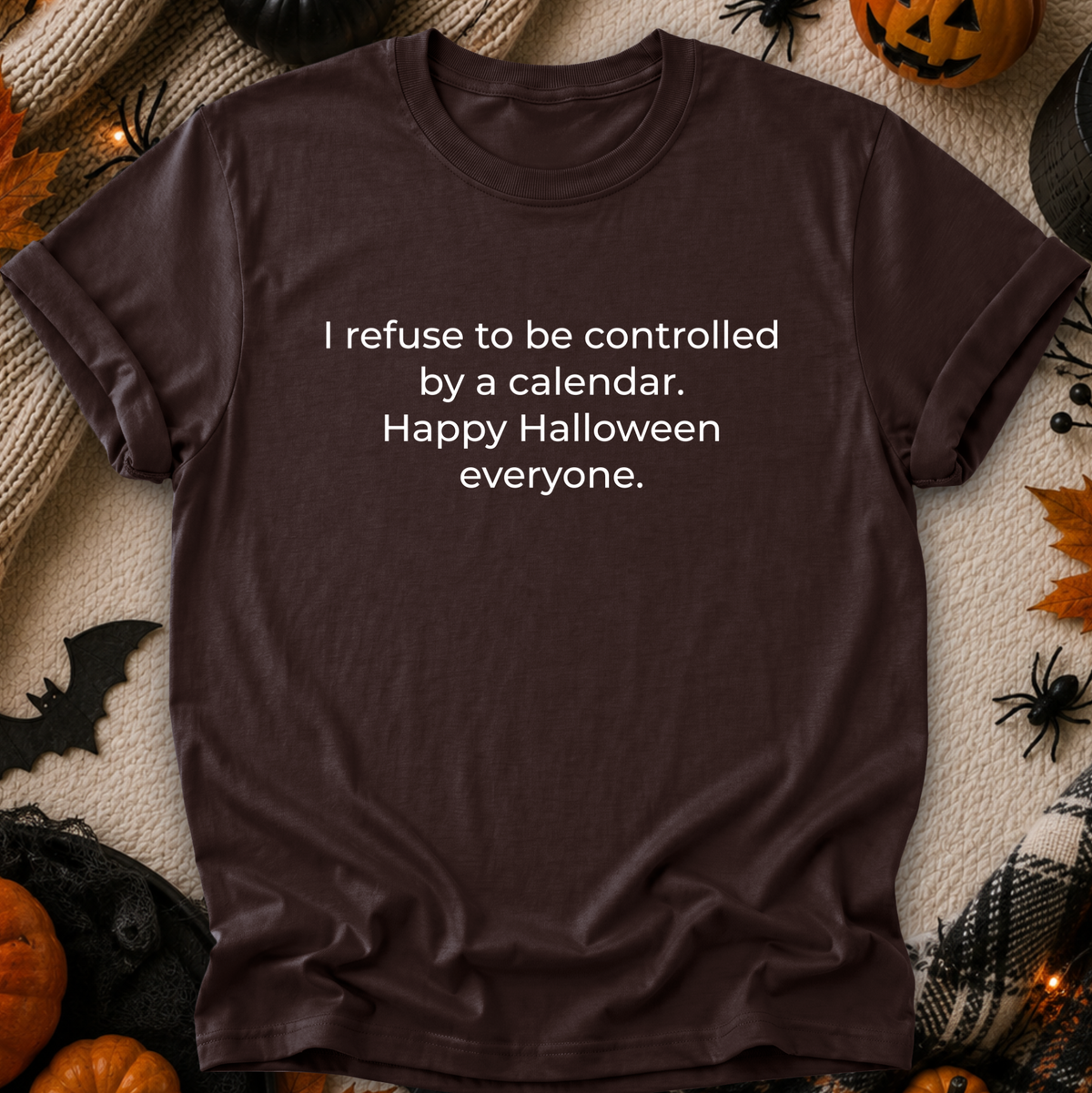 A dark brown short-sleeve t-shirt with white text reading 'I refuse to be controlled by a calendar. Happy Halloween everyone.