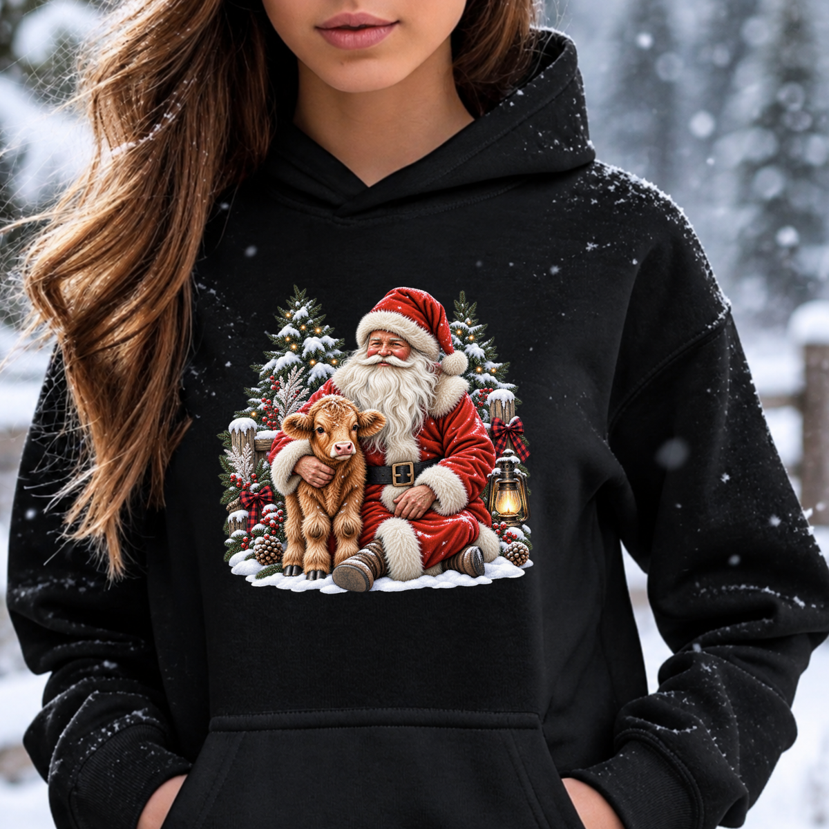 A woman wearing a black pullover hoodie with a large, colorful graphic print of Santa Claus hugging a calf in a snowy Christmas scene. The background is a blurred outdoor winter landscape.