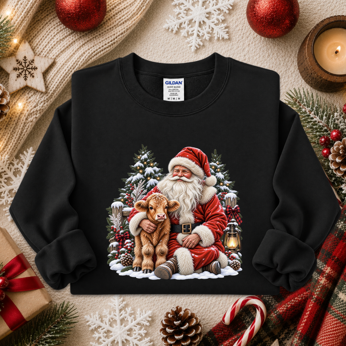 A black crewneck sweatshirt featuring a festive graphic of Santa Claus hugging a calf in a snowy Christmas tree scene. The sweatshirt is displayed in a styled flat-lay arrangement with holiday decorations including pine branches, candy canes, a candle, and a knitted scarf.