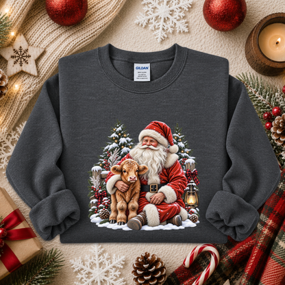 A dark gray crewneck sweatshirt featuring a colorful graphic of Santa Claus hugging a calf in a snowy Christmas tree scene. The sweatshirt is displayed in a flat-lay arrangement with holiday props including pinecones, candy canes, a knitted scarf, and red ornaments.