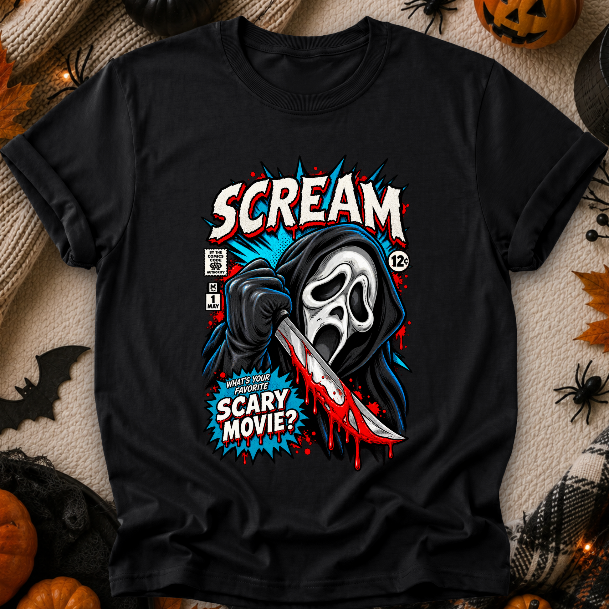 A black graphic t-shirt featuring a stylized comic-book illustration of the Scream character holding a knife, with the text 'SCREAM' and 'WHATS YOUR FAVORITE SCARY MOVIE?'. The shirt is displayed in a flat-lay arrangement with Halloween decorations including pumpkins, a spider, and a bat on a textured beige background.