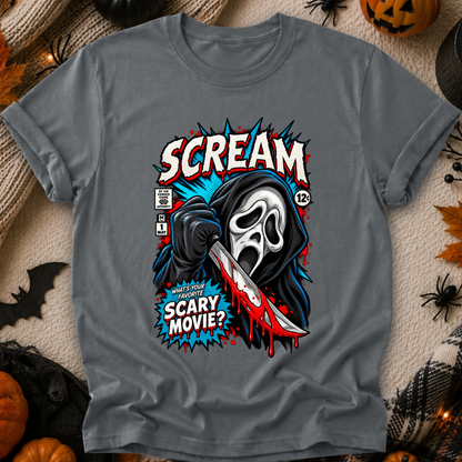 A gray short-sleeve graphic T-shirt laid flat on a cozy beige fabric background with Halloween props. The shirt features a large comic-style print of the Scream character holding a knife, with the words “SCREAM” and “SCARY MOVIE?” in bold red, white, blue, and black.