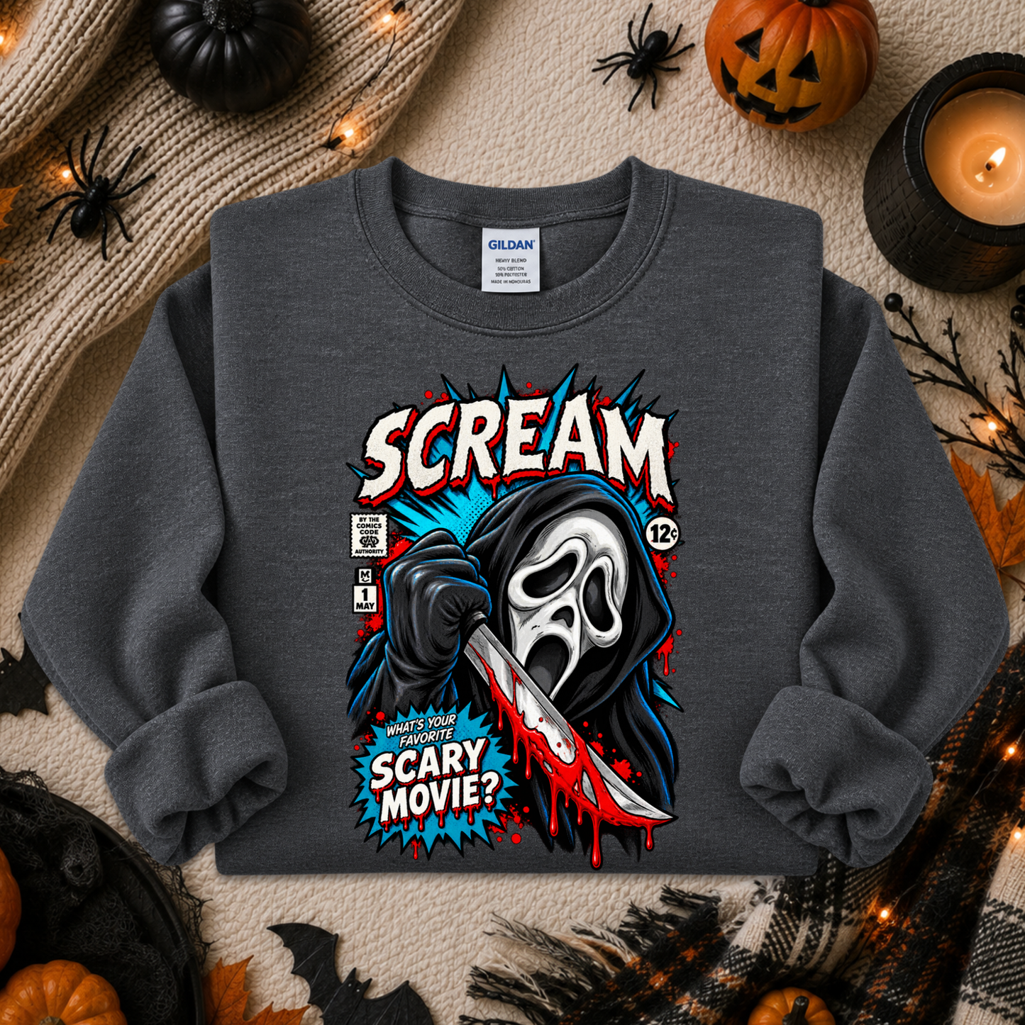 A dark gray crewneck sweatshirt featuring a comic-style graphic of Ghostface holding a bloody knife, with the text 'SCREAM' and 'SCARY MOVIE?'. The sweatshirt is displayed in a flat-lay Halloween setting with pumpkins, a candle, and spider decorations.
