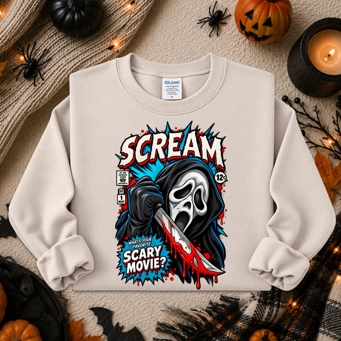 A cream-colored crewneck sweatshirt featuring a comic-style graphic of Ghostface from Scream holding a bloody knife, with the text 'SCREAM' and 'SCARY MOVIE?'. The sweatshirt is styled in a flat-lay on a cozy autumn background with pumpkins, a candle, and a knitted sweater.