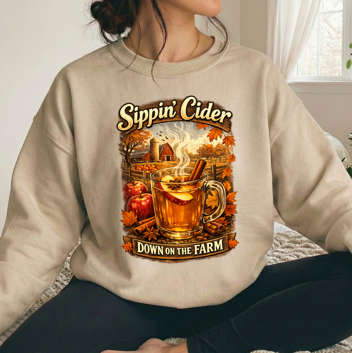 woman wearing a beige sweatshirt with fall autumn farm scene with a glass of apple cider graphic that says sippin cider down on the farm