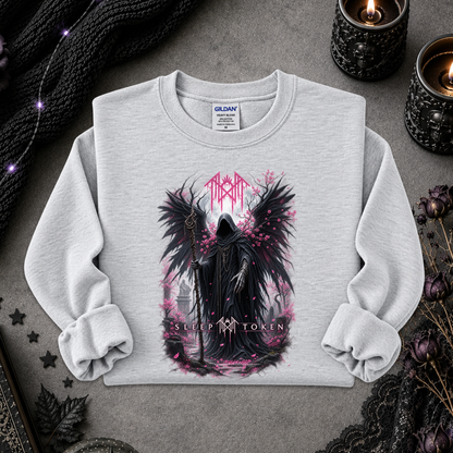 A light gray crewneck sweatshirt featuring a gothic graphic of a winged grim reaper with pink accents and the text 'MARA' and 'SUCCEOR TOKEN'. The sweatshirt is styled in a flat-lay on a dark gray textured surface with gothic props including a black knit sweater, candles, and dried flowers.