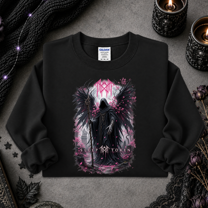 A black crewneck sweatshirt with a gothic graphic of a dark angel figure and pink accents, styled flat-lay on a gray textured surface with candles, lace, and a knit blanket.