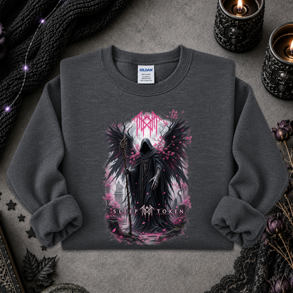 A dark gray crewneck sweatshirt with a gothic graphic of a winged hooded figure and pink blossoms, styled flat-lay on a textured gray surface with candles, lace, and black knit fabric.