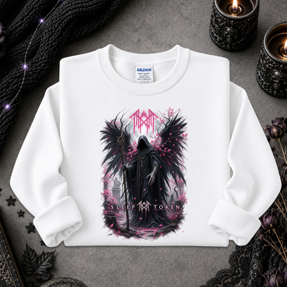 A white long-sleeve crewneck sweatshirt with a gothic graphic of a winged dark figure and pink text, laid flat on a gray surface with candles and black lace props.