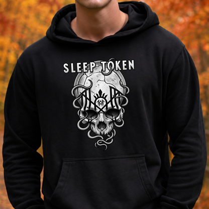 A person wearing a black pullover hoodie with a large white and gray graphic on the chest featuring the text 'SLEEP TOKEN' above a stylized skull and snake design, set against an out-of-focus autumn background.