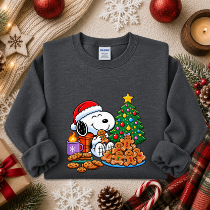 A dark gray crewneck sweatshirt featuring a colorful graphic of Snoopy and Woodstock by Christmas, styled in a cozy holiday flat-lay with a knit sweater, candles, ornaments, and candy canes.