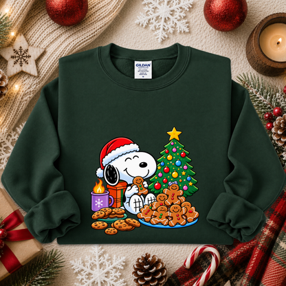 A dark green crewneck sweatshirt featuring a colorful graphic of Snoopy and Woodstock by Christmas, styled in a cozy holiday flat-lay with a knit blanket, candles, ornaments, and candy canes.