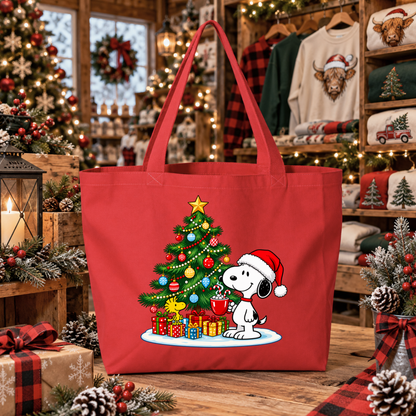 A red canvas tote bag featuring a festive Christmas graphic of Snoopy sitting next to a decorated tree with presents, displayed on a wooden table in a cozy, decorated holiday shop setting.