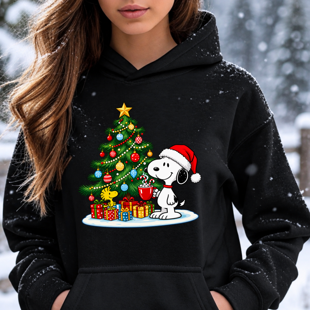 A woman wearing a black hoodie with a festive Christmas graphic of Snoopy and Woodstock decorating a tree, set against a snowy outdoor background.