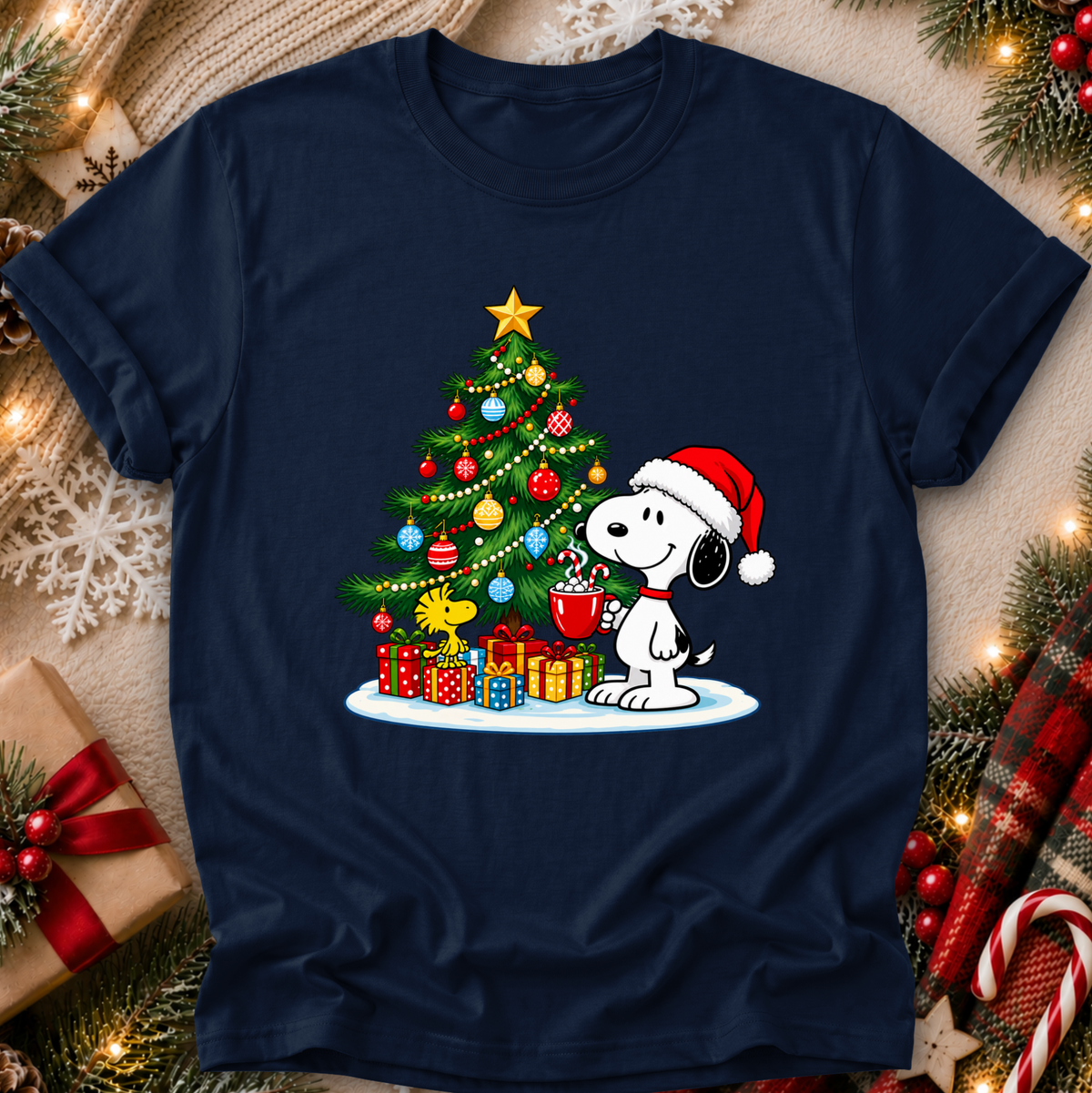 A navy blue crewneck t-shirt featuring a festive graphic of Snoopy and Woodstock by the Christmas tree, surrounded by holiday decorations like pine branches, ornaments, and wrapped gifts.
