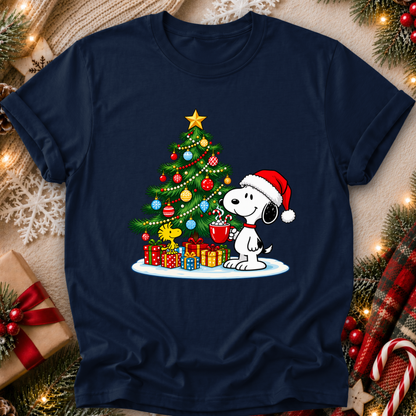 A navy blue crewneck t-shirt featuring a festive graphic of Snoopy and Woodstock by the Christmas tree, surrounded by holiday decorations like pine branches, ornaments, and wrapped gifts.