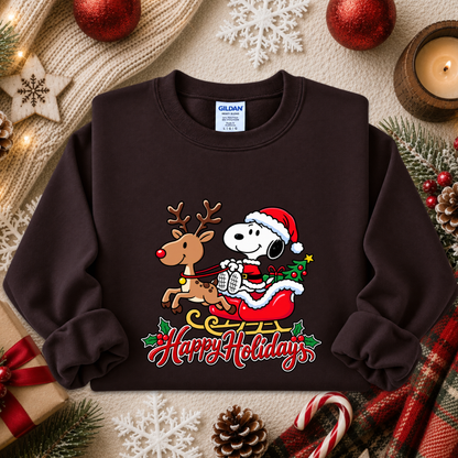 A dark brown crewneck sweatshirt featuring a colorful graphic of Snoopy in a Santa hat and sleigh with a reindeer, surrounded by holiday decorations like pine branches, ornaments, and a candle. The text 'Happy Holidays' is printed below the graphic.