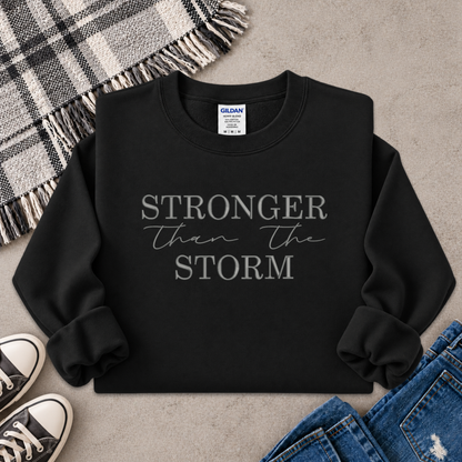 black sweatshirt with the text Stronger Than The Storm embroidered on it