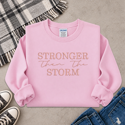 light pink sweatshirt with the text Stronger Than The Storm embroidered on it