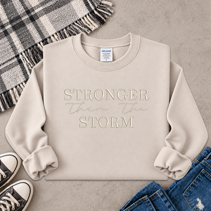 beige sweatshirt with the text Stronger Than The Storm embroidered on it