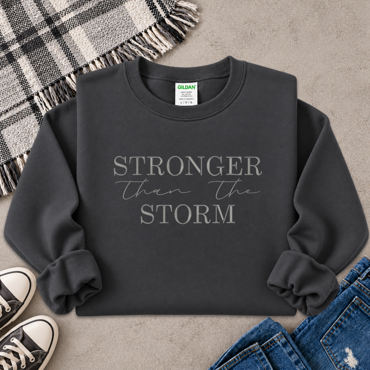 gray sweatshirt with the text Stronger Than The Storm embroidered on it