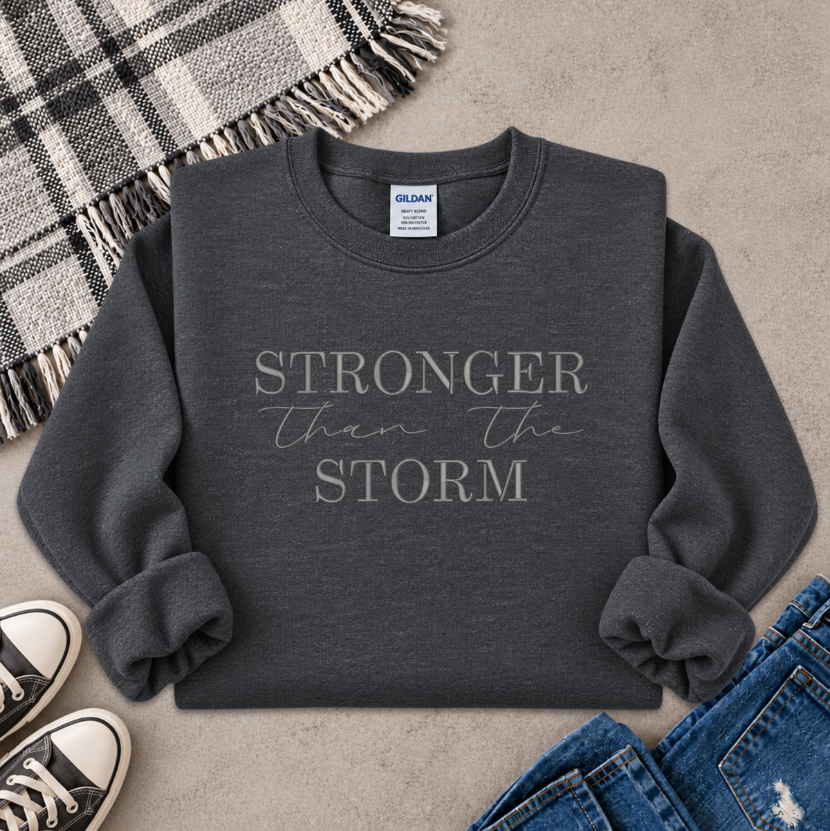 gray sweatshirt with the text Stronger Than The Storm embroidered on it