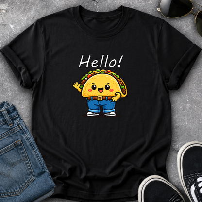 A black short-sleeve graphic T-shirt laid flat on a gray textured surface, styled with blue jeans, sunglasses, and black sneakers. The shirt features a cartoon taco character wearing blue pants and white sneakers, with the word 'Hello!' printed above in white.