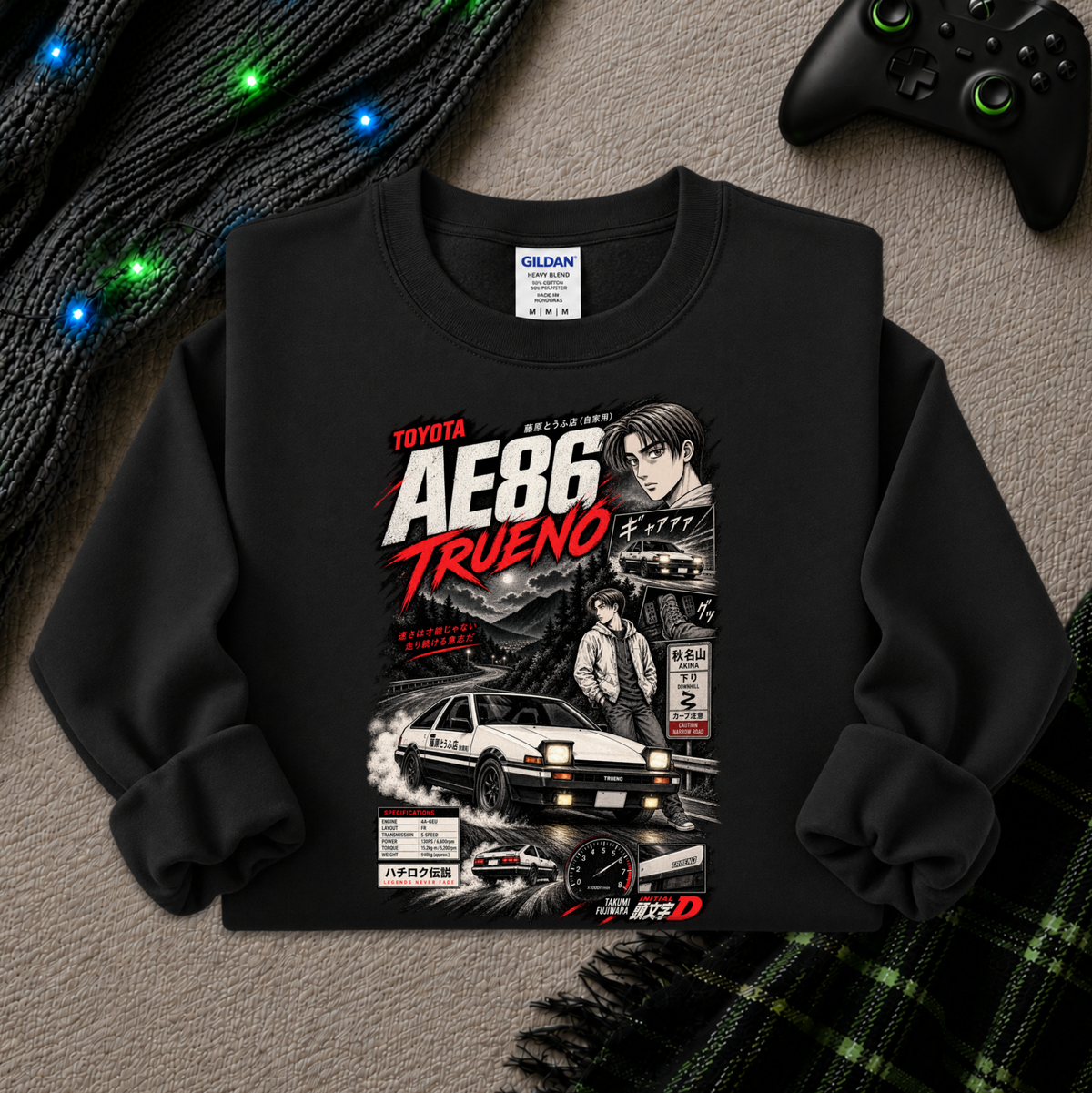 A black long-sleeve crewneck sweatshirt with a detailed graphic print of the Toyota AE86 Trueno from the movie Initial D, styled flat on a gray textured background with a black knit sweater, glowing fairy lights, and a black game controller.