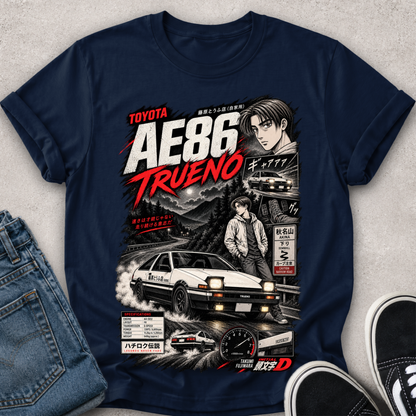 A navy blue graphic t-shirt featuring a detailed print of the Toyota AE86 Trueno from the movie Initial D, styled in a flat-lay with blue jeans and black sneakers on a textured gray background.