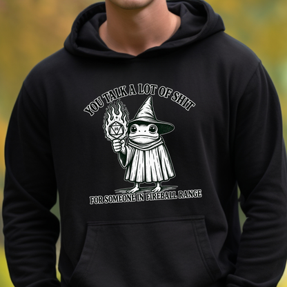 A person wearing a black pullover hoodie with a white graphic print on the chest. The graphic shows a cartoon wizard holding a flame and text that reads 'YOU TALK A LOT OF SHIT FOR SOMEONE IN FIREBALL RANGE'.