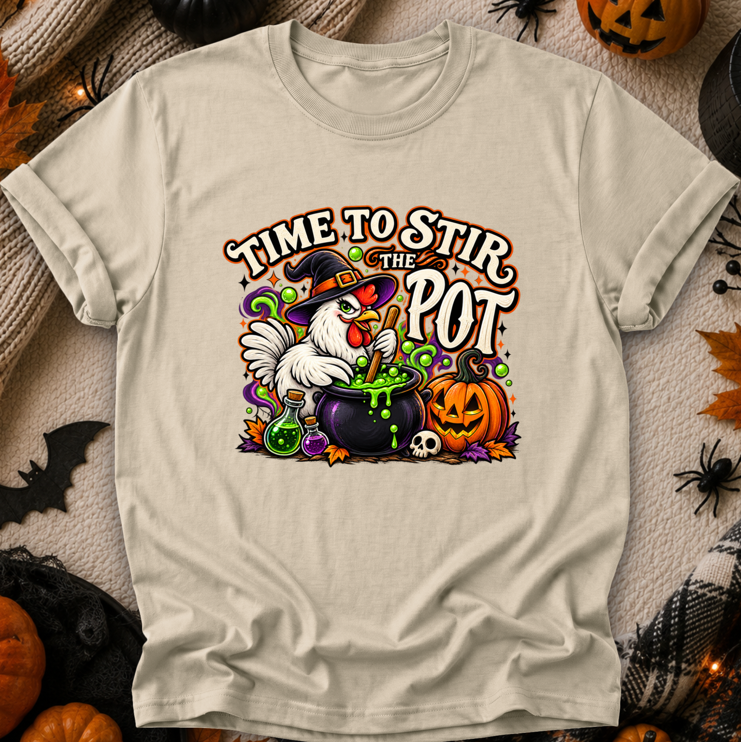 A light beige graphic t-shirt featuring a Halloween-themed illustration of a white chicken in a witch hat stirring a cauldron of green potion next to a jack-o'-lantern pumpkin. The text reads 'TIME TO STIR THE POT'.