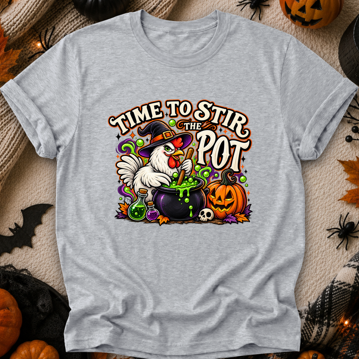 A light heather gray short-sleeve t-shirt with a colorful Halloween graphic of a white rooster in a witch hat stirring a cauldron of green potion next to a jack-o'-lantern pumpkin. The text reads 'TIME TO STIR THE POT'.