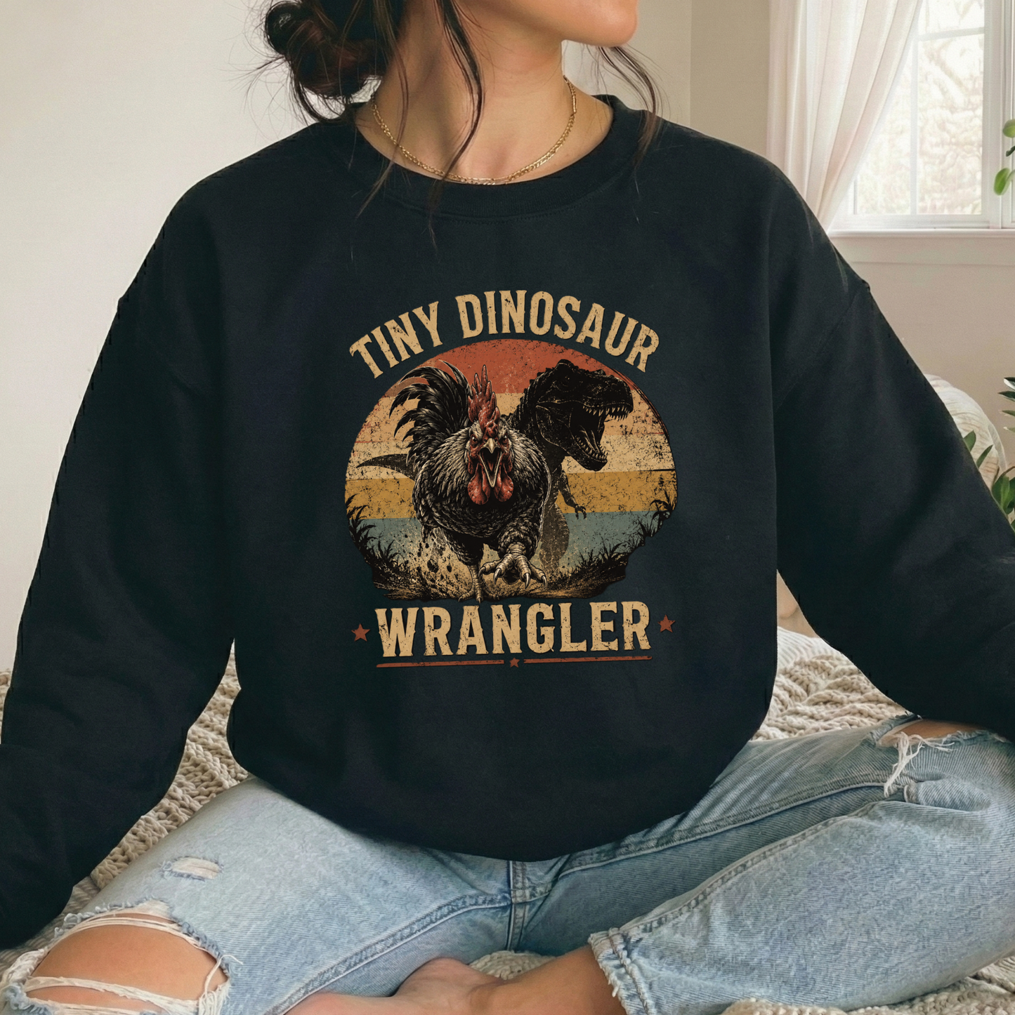 woman wearing a black sweatshirt with a distressed graphic of a angry chicken and dinosaur that says tiny dinosaur wrangler