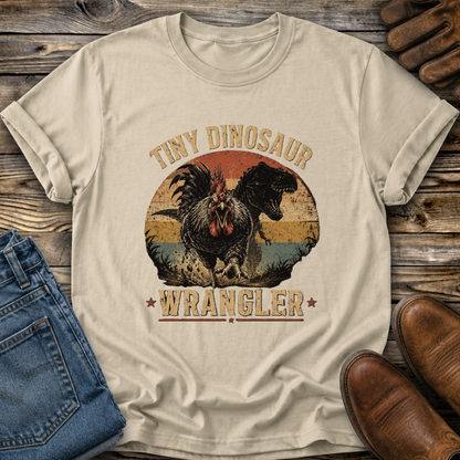 beige tshirt with a distressed graphic of a angry chicken and dinosaur that says tiny dinosaur wrangler
