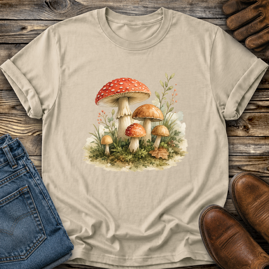 A beige crewneck t-shirt featuring a vintage-style graphic print of red-capped mushrooms and small wildflowers on the front, displayed against a light gray background.