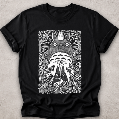 A black short-sleeve crewneck t-shirt featuring a detailed black and white graphic print of Totoro and other My Neighbor Totoro characters surrounded by foliage, laid flat on a textured light gray background.