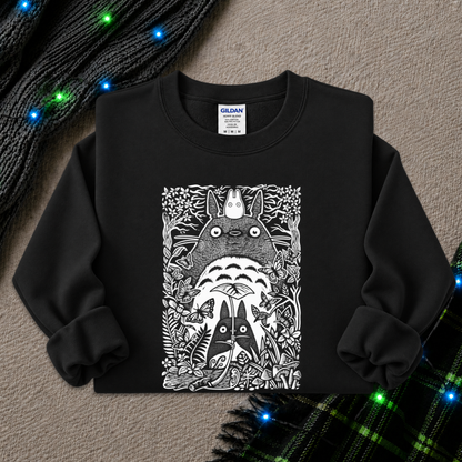 A black long-sleeve crewneck sweatshirt featuring a detailed black and white graphic of Totoro and other My Neighbor Totoro characters, styled flat on a textured gray background with holiday lights and a plaid scarf.