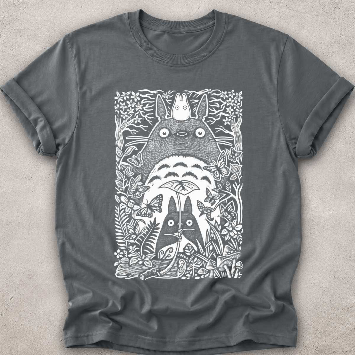 A dark gray crewneck t-shirt featuring a detailed white line art graphic of Totoro and other My Neighbor Totoro characters surrounded by foliage, laid flat on a textured light gray background.