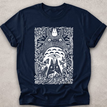 A navy blue short-sleeve crewneck t-shirt featuring a detailed white line art graphic of Totoro and other My Neighbor Totoro characters surrounded by foliage, laid flat on a textured light gray background.