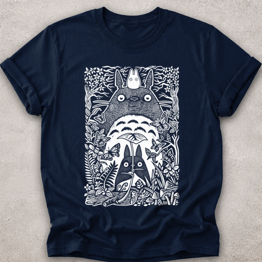 A navy blue short-sleeve crewneck t-shirt featuring a detailed white line art graphic of Totoro and other My Neighbor Totoro characters surrounded by foliage, laid flat on a textured light gray background.