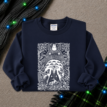 A navy blue Gildan sweatshirt featuring a detailed black and white graphic of Totoro and other My Neighbor Totoro characters, styled flat on a textured beige background with holiday lights and plaid fabric accents.