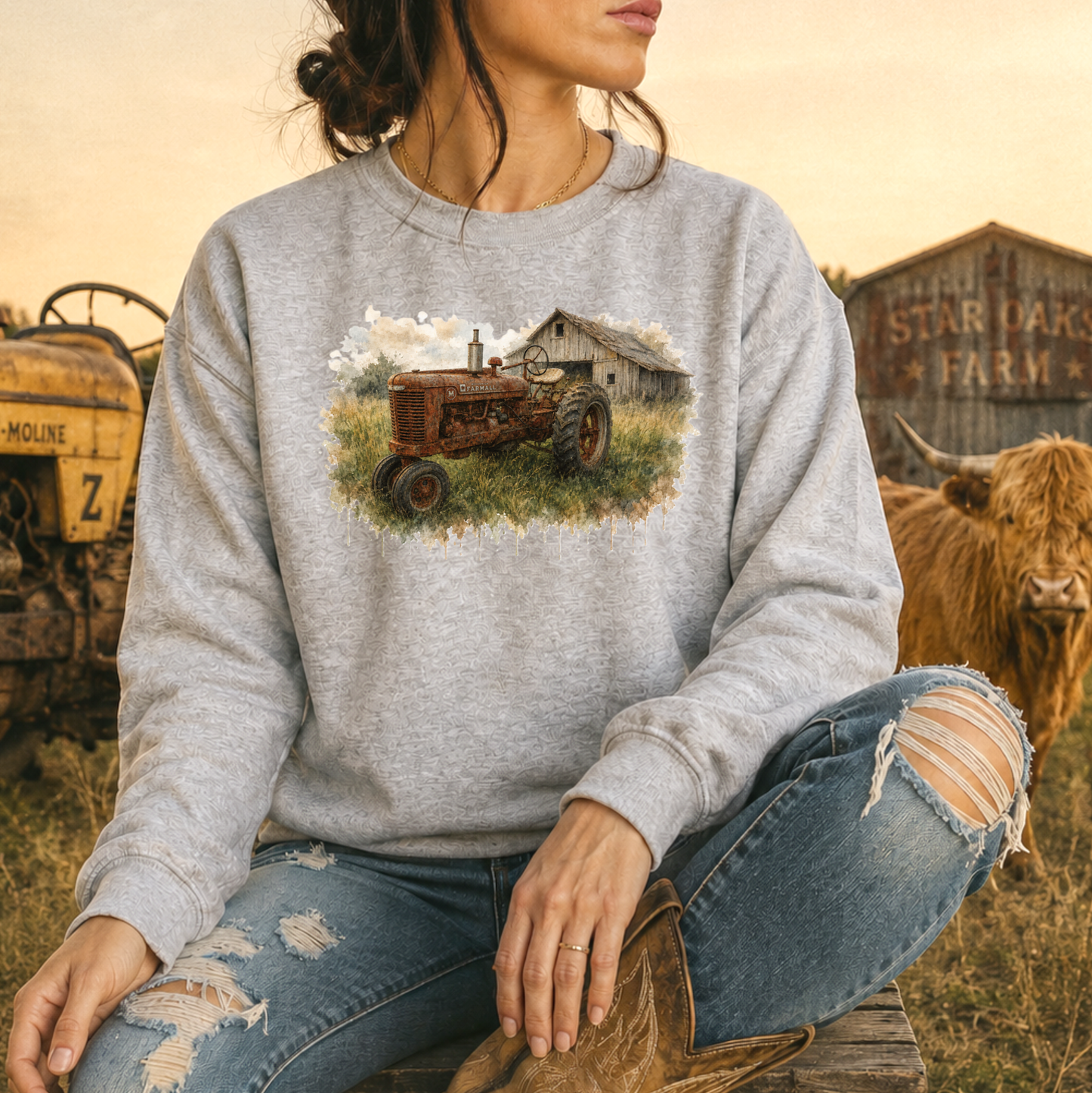 woman wearing a gray sweatshirt with a watercolor barn and rusty farmall tractor farm scene graphic on it