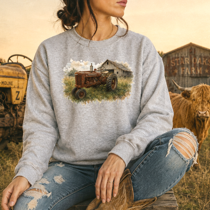 woman wearing a gray sweatshirt with a watercolor barn and rusty farmall tractor farm scene graphic on it