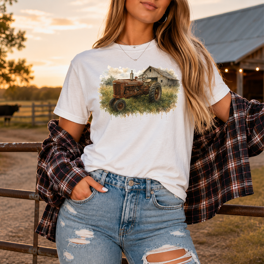 woman wearing a white tshirt with a watercolor barn and rusty farmall tractor farm scene graphic on it