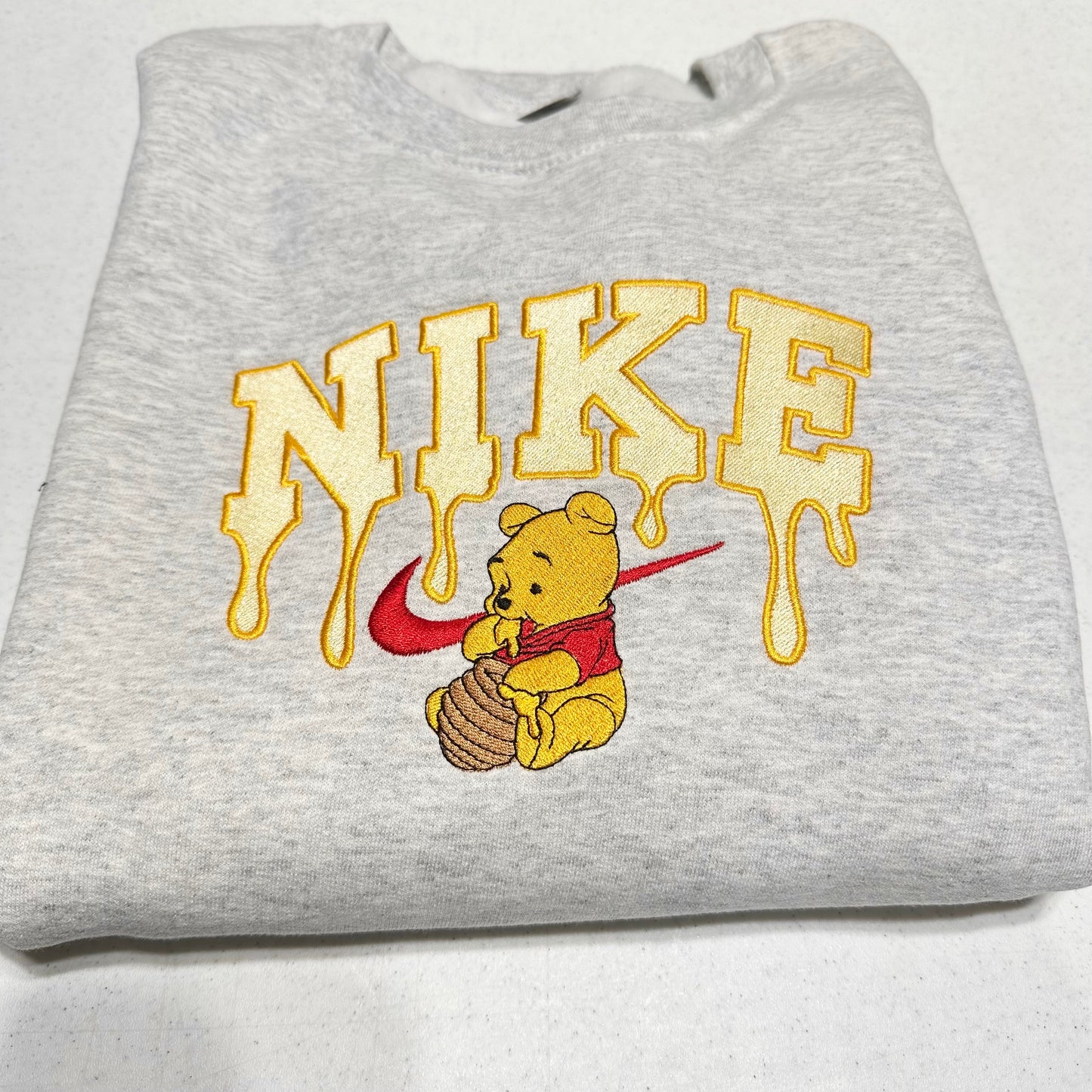 gray sweatshirt with embroidered winnie the pooh with honey dripping from the nike logo