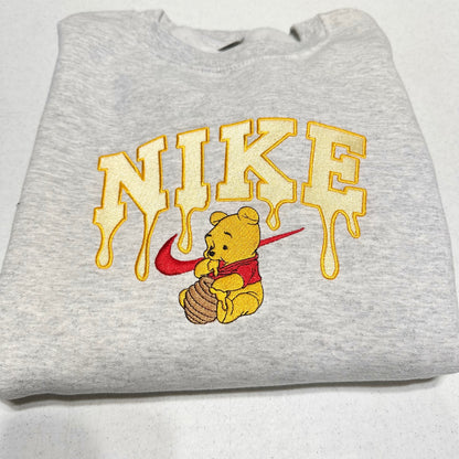gray sweatshirt with embroidered winnie the pooh with honey dripping from the nike logo